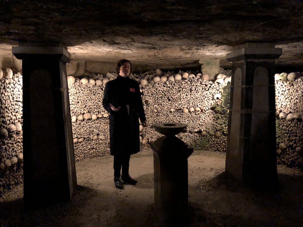 Paris Catacombes tour guide in front of wall of bones