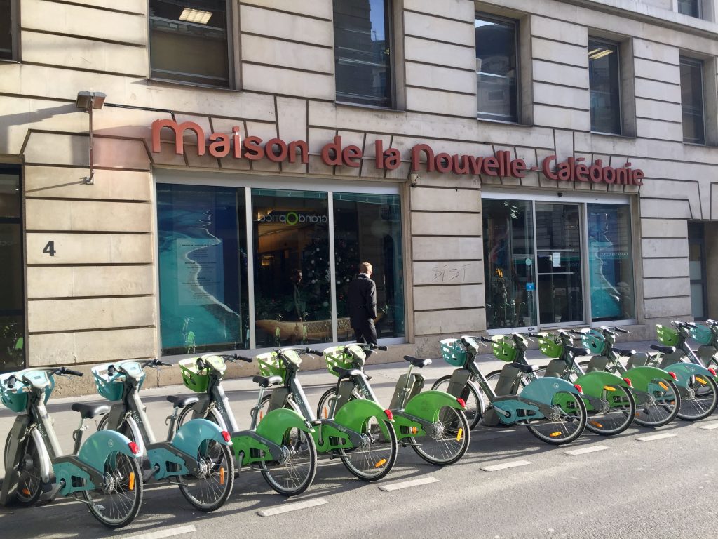 Paris green and blue Vélib city bikes lined up in from of Maison de la Nouvelle-Calédonie