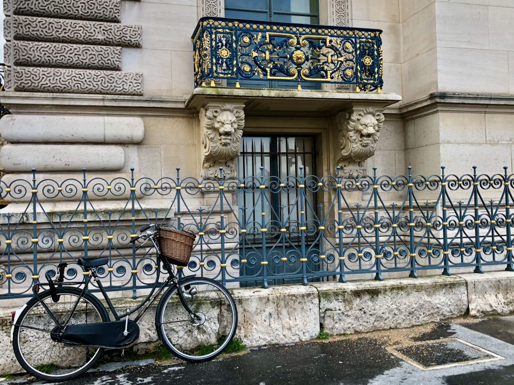 gold detailing on wrought iron railing on a Paris building, bike leaning against a fence