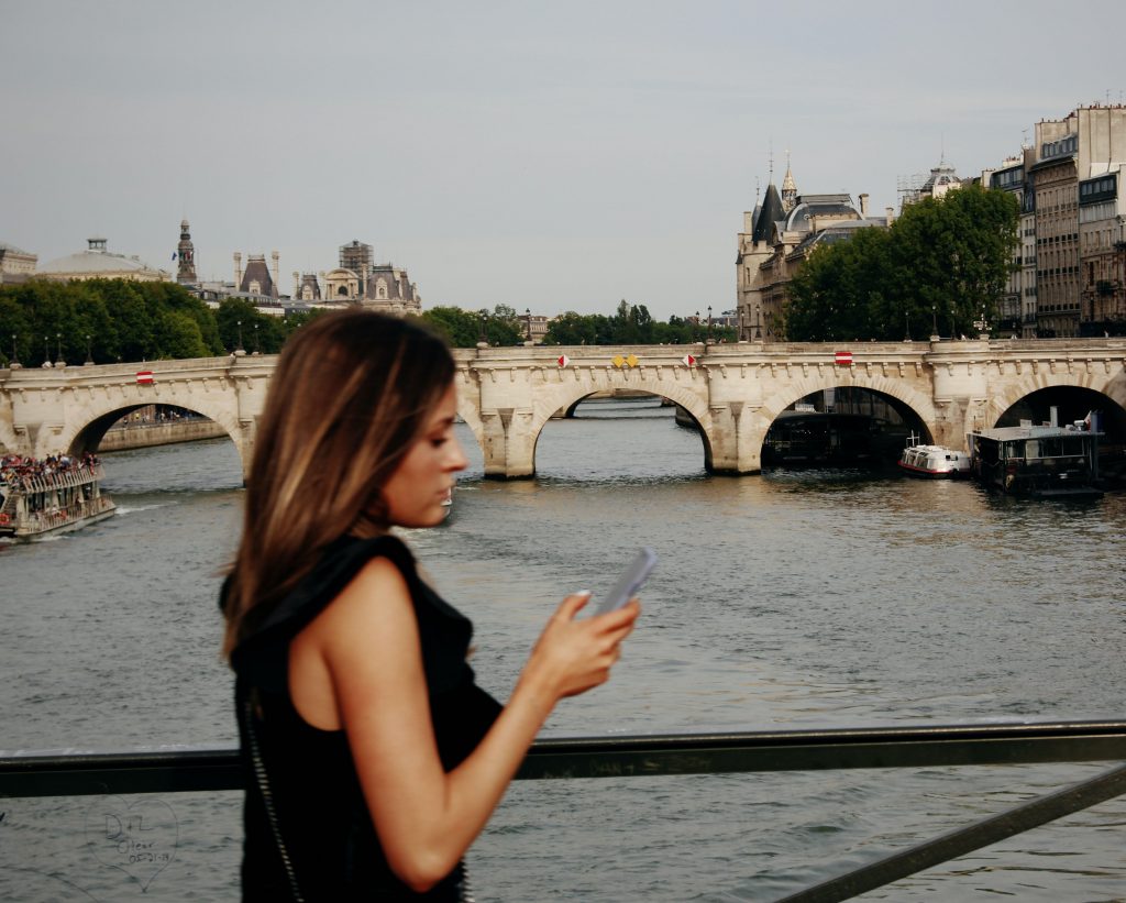a woman checking her phone while walking across a bridge in Paris