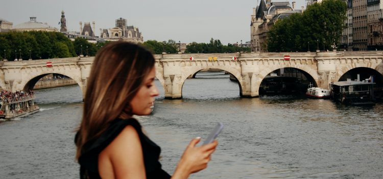 a woman checking her phone while walking across a bridge in Paris
