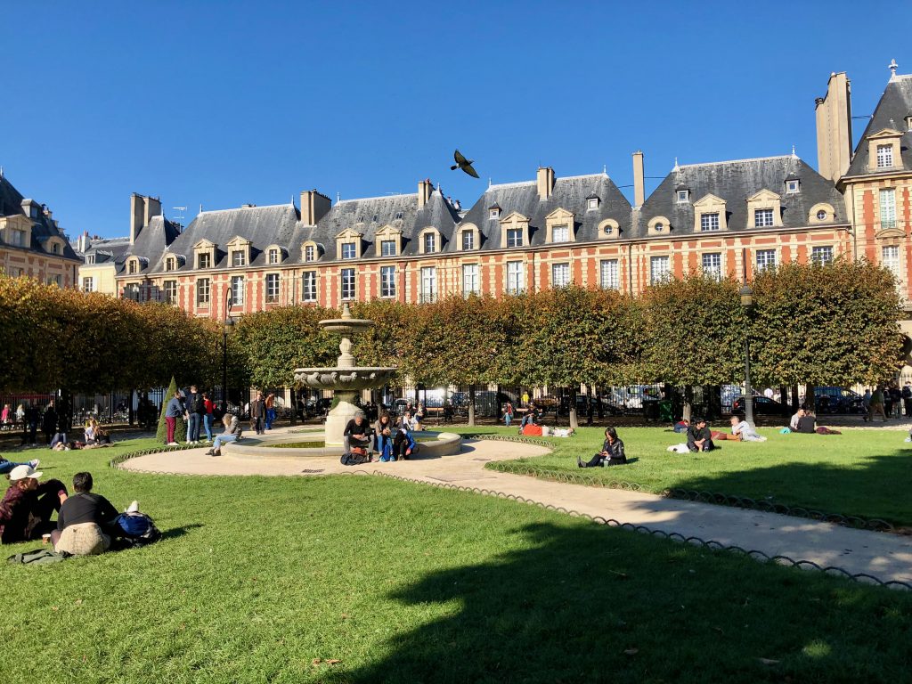 people enjoying a beautiful day on the green grass at Place des Vosges