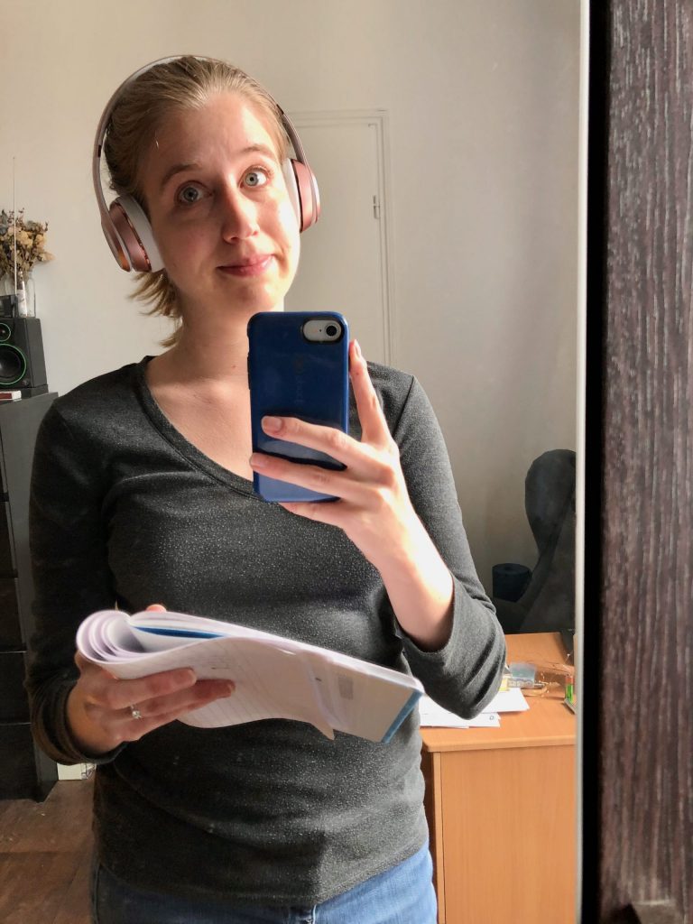 women holding a notebook and wearing headphones on a phone call, taking a selfie in the mirror