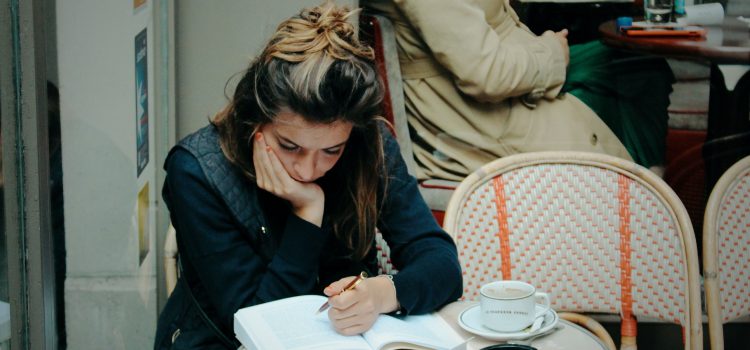 girl reading on a Paris café terrace with a coffee, pack of cigarettes, and ashtray on the table