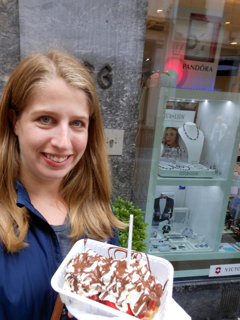 woman holding a to-go plate of waffles piled high with strawberries, whipped cream, and chocolate sauce in Brussels