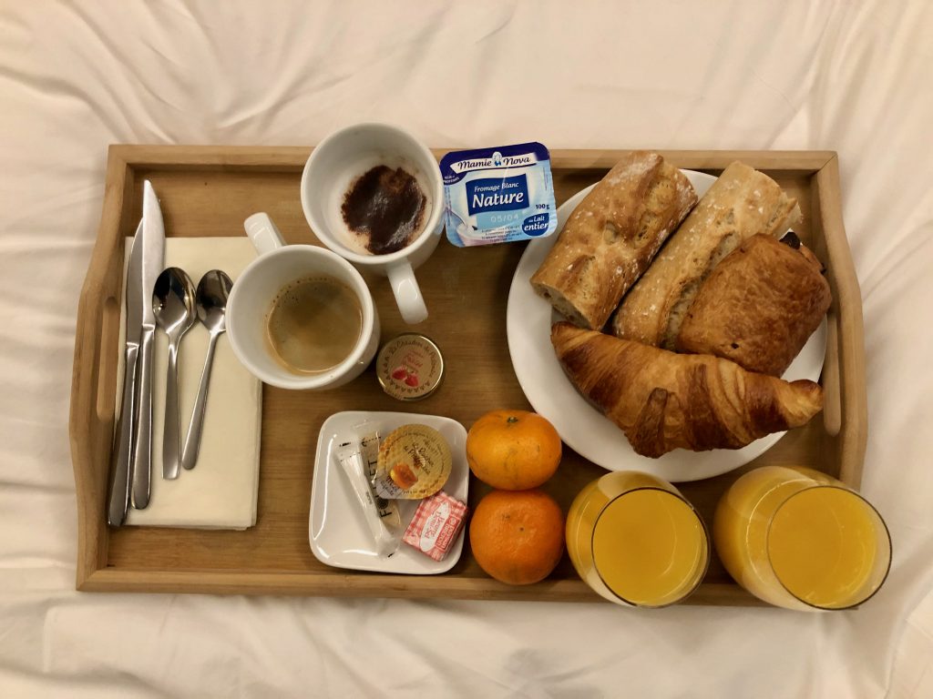 a typical breakfast in France ordered as room service in a French hotel served on a wooden tray: 1 latte and 1 black coffee, 2 glasses of orange juice, 1 croissant, 1 pain au chocolat, slices of baguette (tartines), 1 yogurt, butter, jam, and 2 mandarin oranges