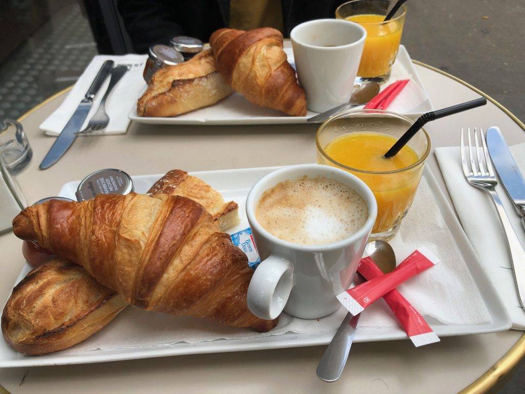 a typical breakfast in France ordered as a formule from a French café in Paris: croissant, baguette (tartine), cup of coffee, glass of orange juice, butter, and jam