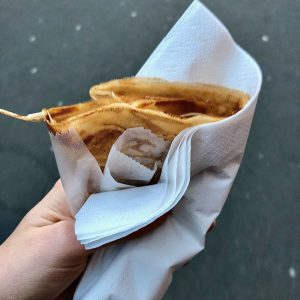 simple crêpe held in a napkin, sidewalk in the background