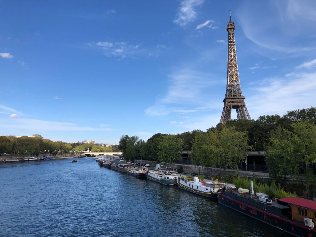 boats lined up along the banks of the Seine River and the Eiffel Tower in the background, blue skies