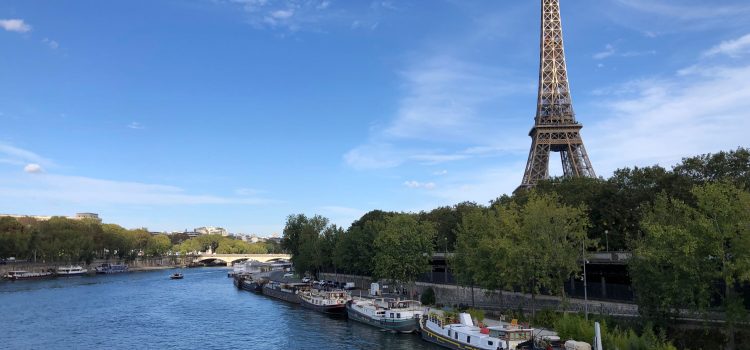 boats lined up along the banks of the Seine River and the Eiffel Tower in the background, blue skies