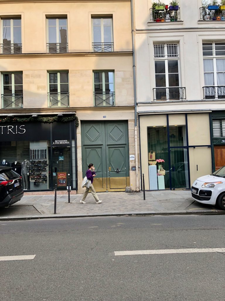 woman walking past a blue-green door in Paris with a small mosaic Invader on the building, to the right of the door