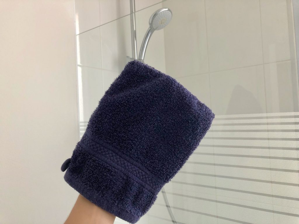 French-style navy blue washcloth mitt with showerhead in the background