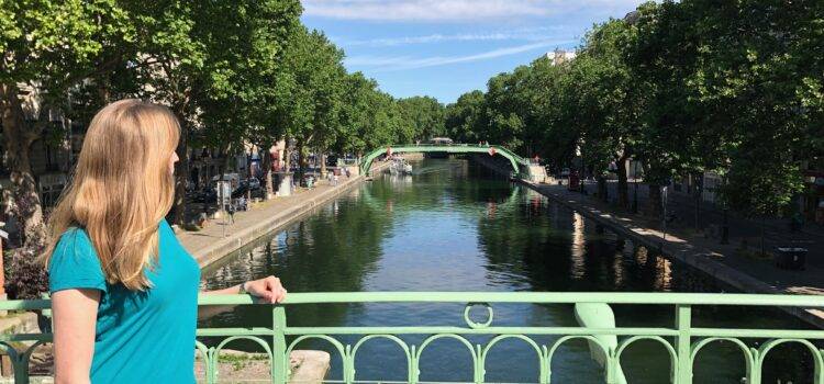 blond woman wearing blue turquoise teeshirt and jeans, looking out over the Canal Saint-Martin on a summer day in Paris