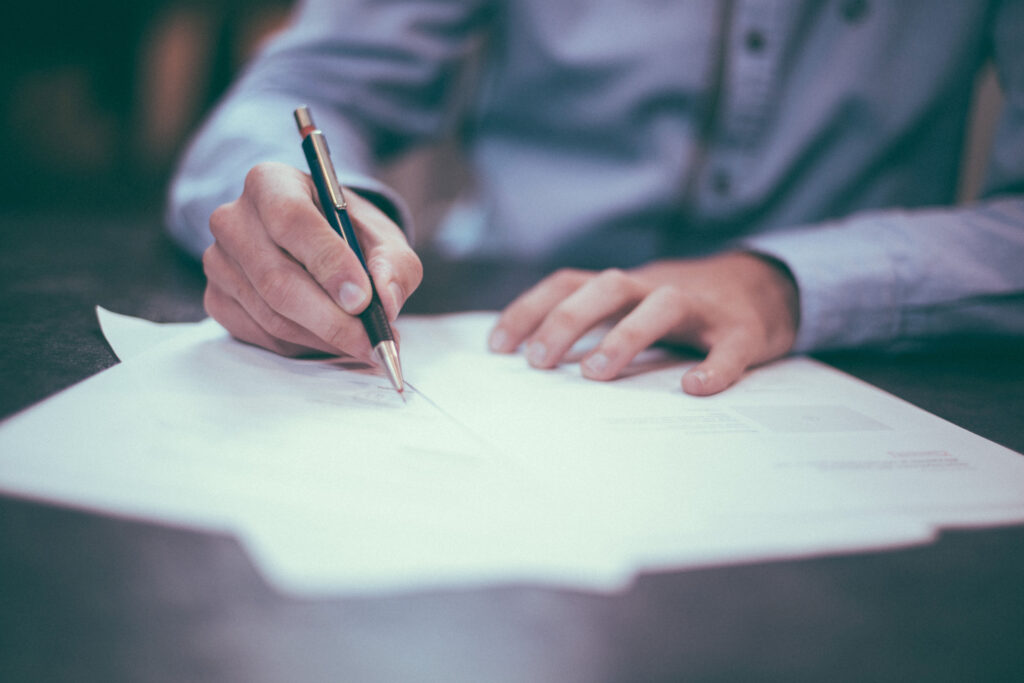 man holding pen and writing on a small pile of papers