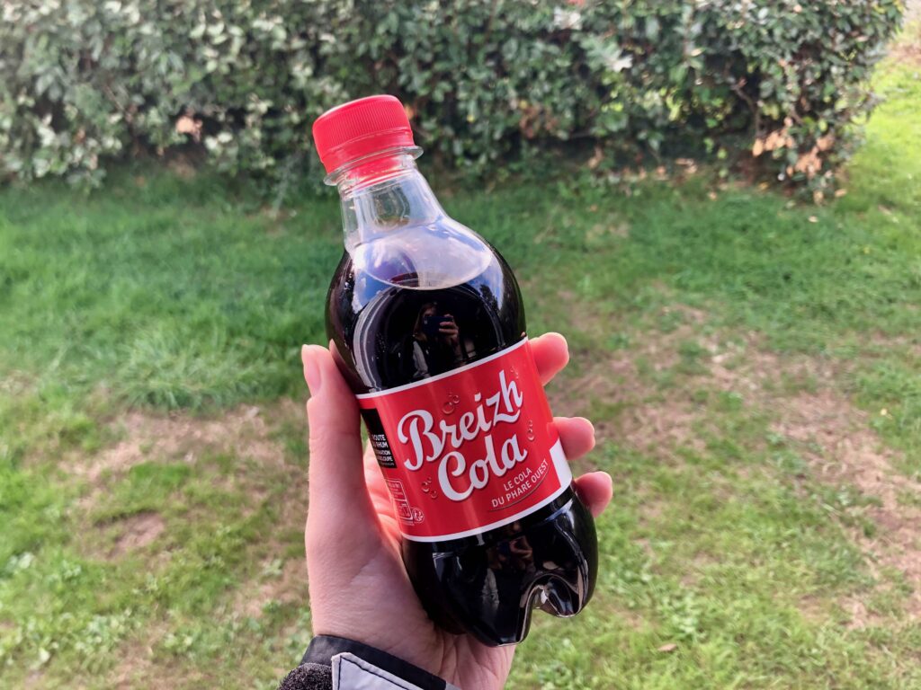 a bottle of Breizh cola, a local cola of Bretagne, held in the hand with green grass in the background