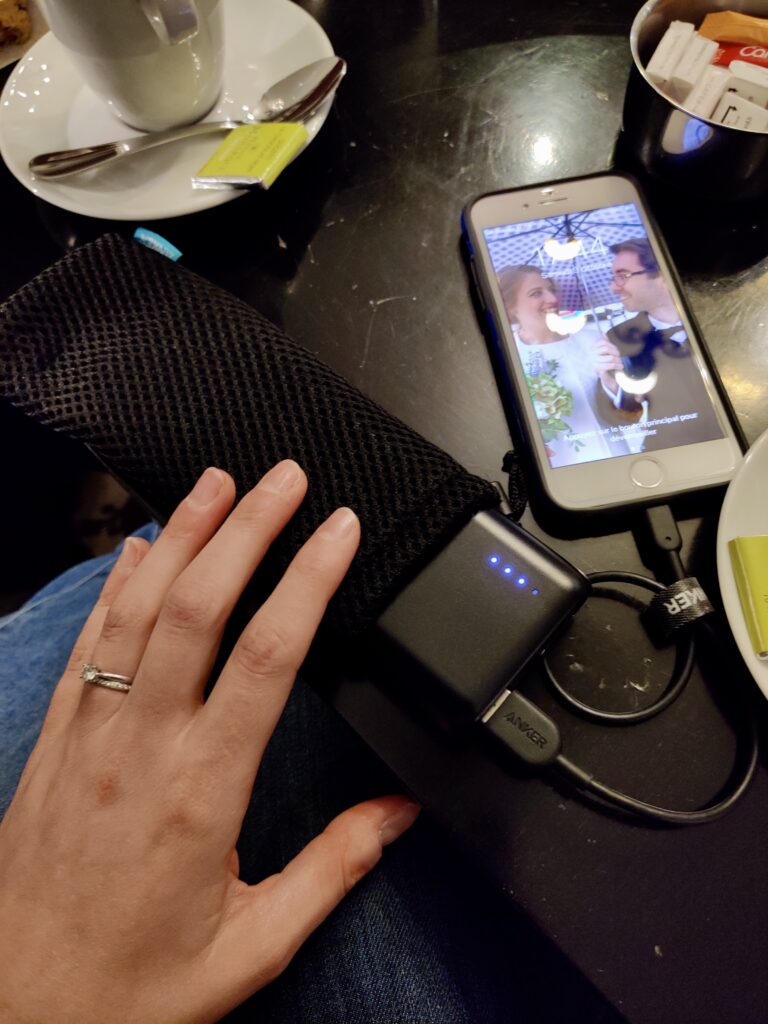 iphone hooked up to portable charger on a table with coffee mugs nearby