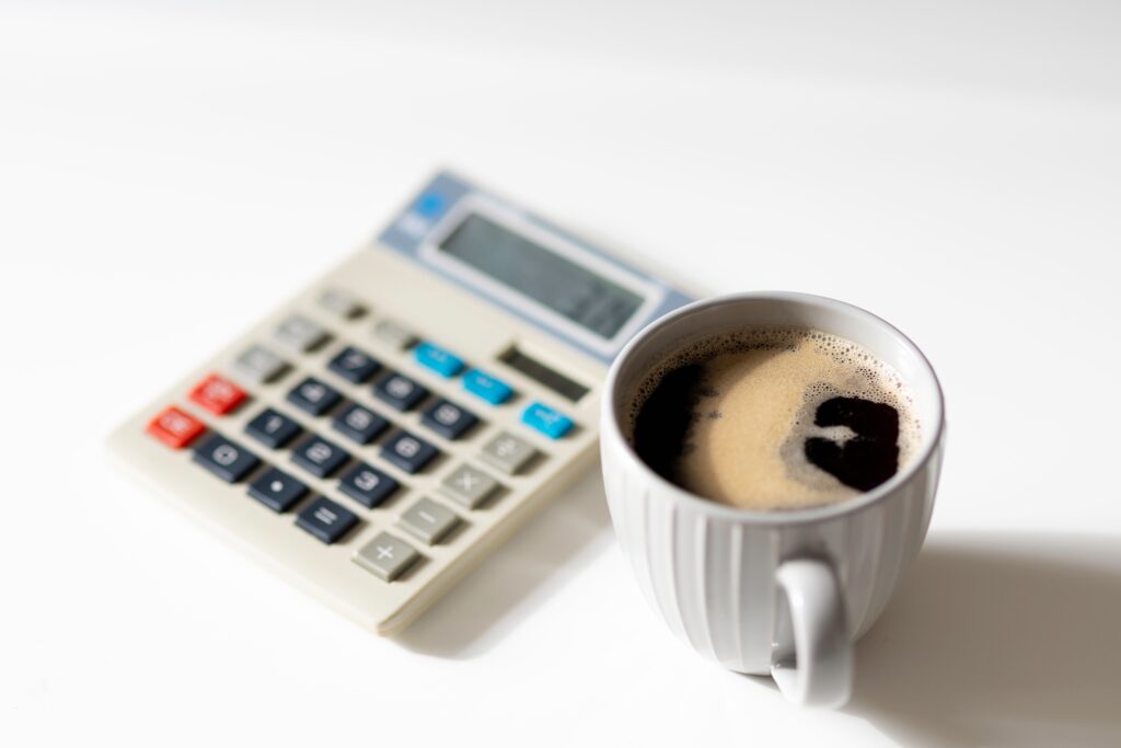 coffee cup with black coffee in the foregound and an out of focus calculator in the background