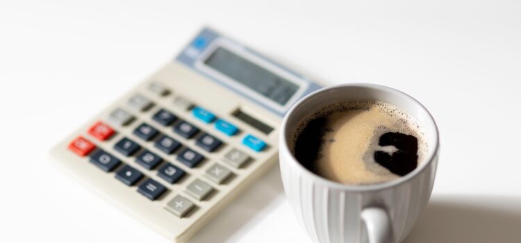 coffee cup with black coffee in the foregound and an out of focus calculator in the background