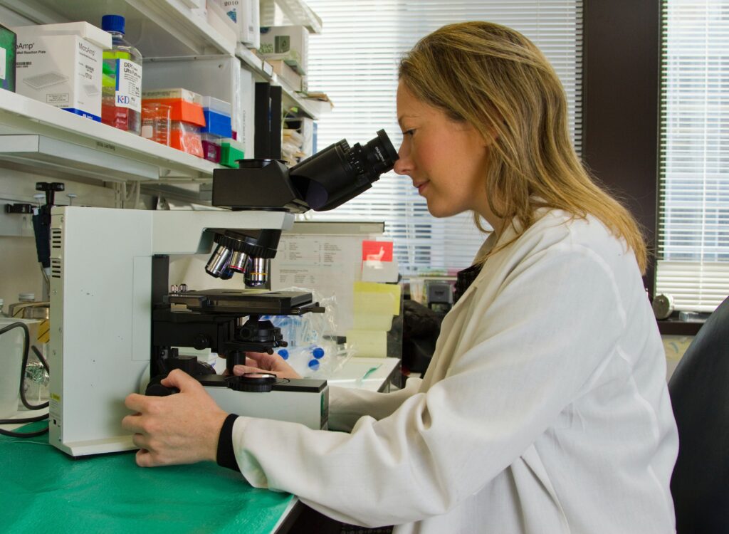 blond woman looking into a microscope, analyzing test results in a lab
