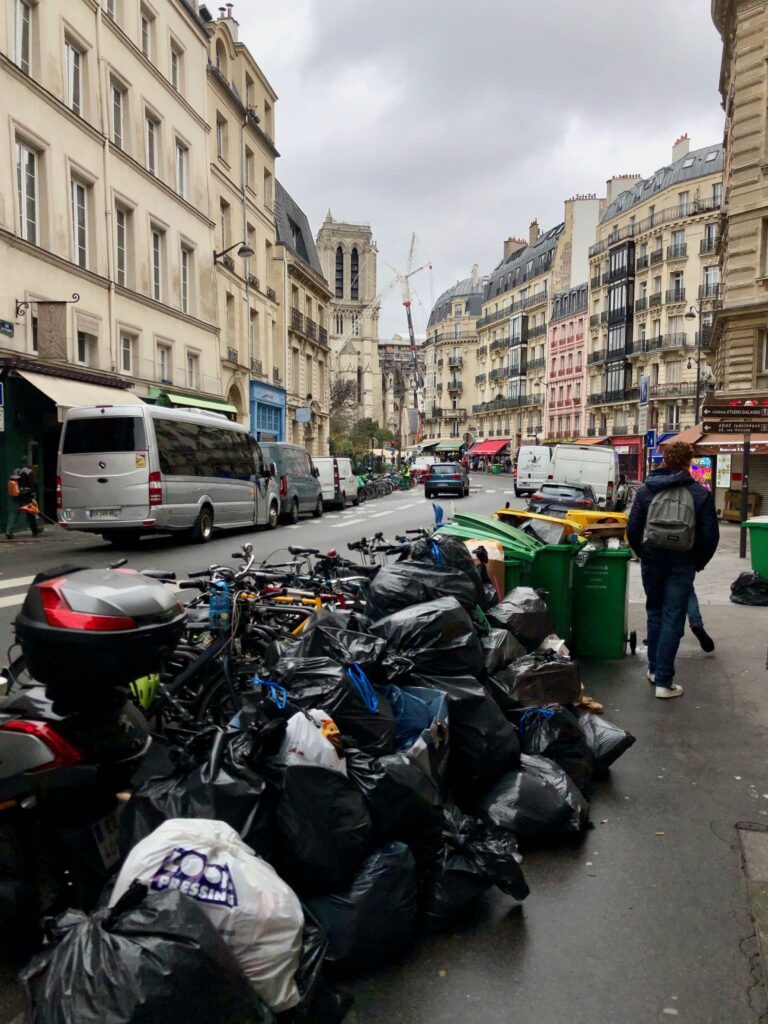 garbage bags piled up on the sidewalk in Paris during the garbage collector strike against retirement forms, Notre Dame in the background