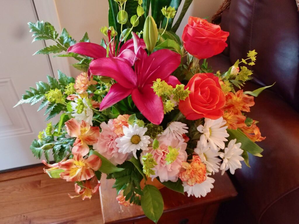 large bouquet of Mother's Day flowers including fuchsia lilies, orange roses, white daisies, light pink carnations, green sprigs of leaves