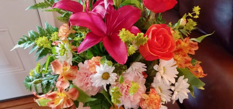 large bouquet of Mother's Day flowers including fuchsia lilies, orange roses, white daisies, light pink carnations, green sprigs of leaves