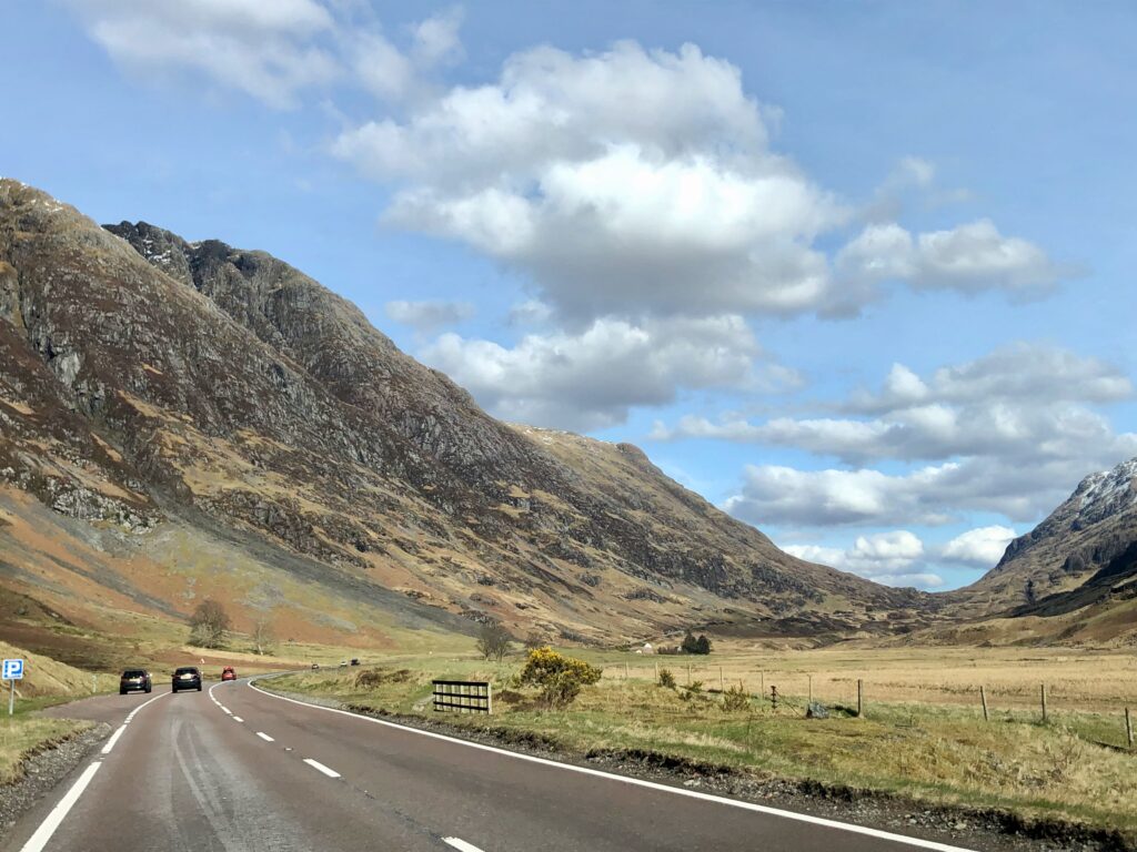 photo taken from the car on the left side of the road in Glencoe Scotland, light blue skies with fluffy clouds