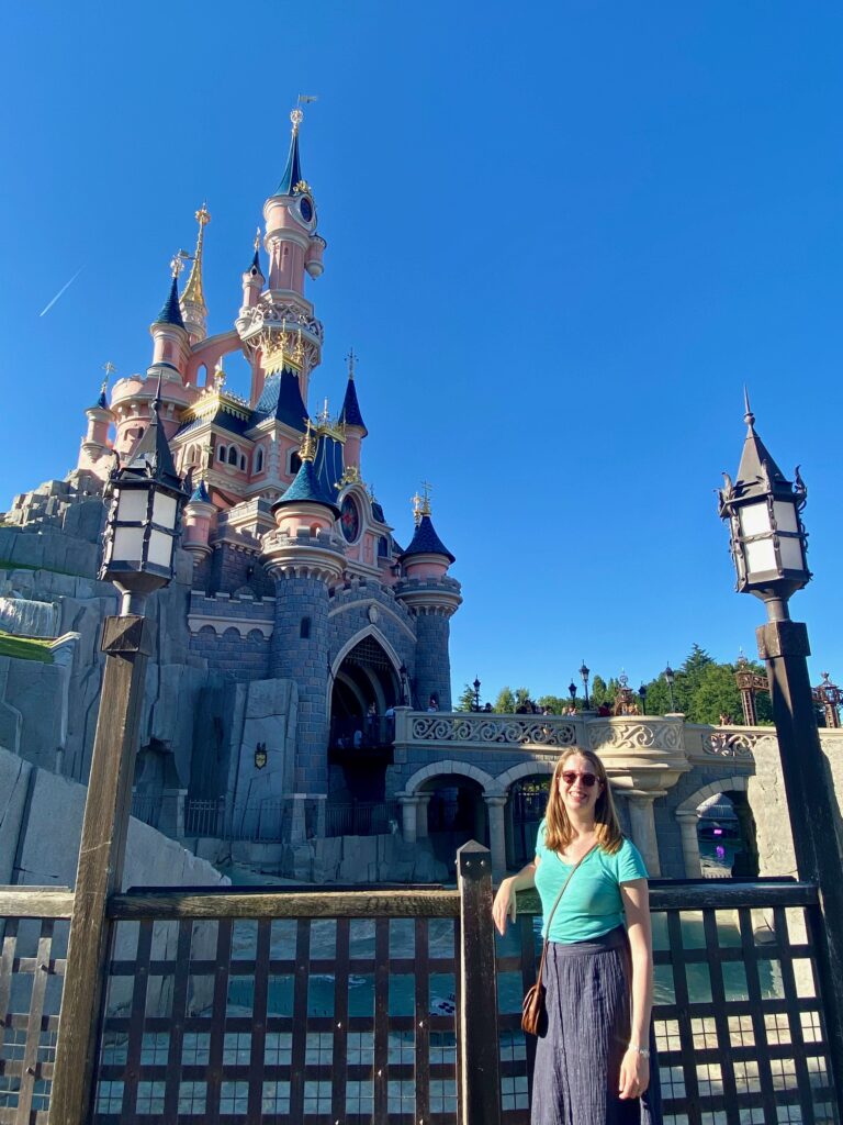 woman standing in front of the Sleeping Beauty Castle in Disneyland Paris on a bright, summer day