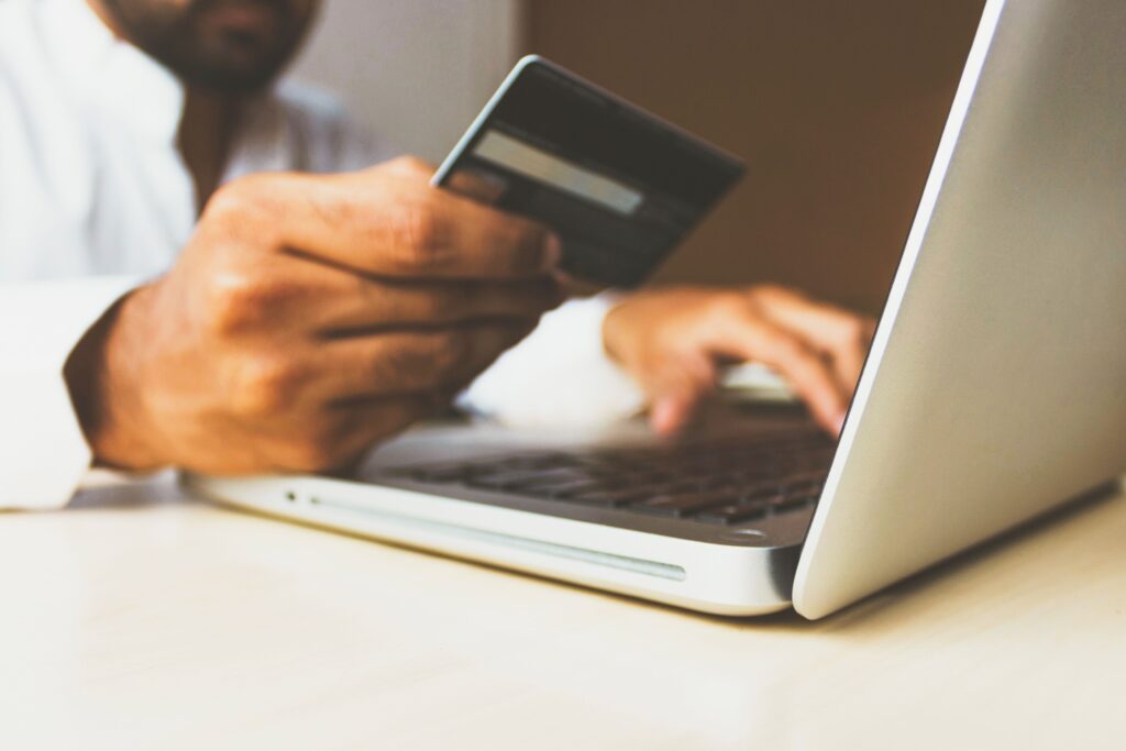 Man making an online payment. He's holding a credit card in his right hand, with his left hand typing on a laptop computer.