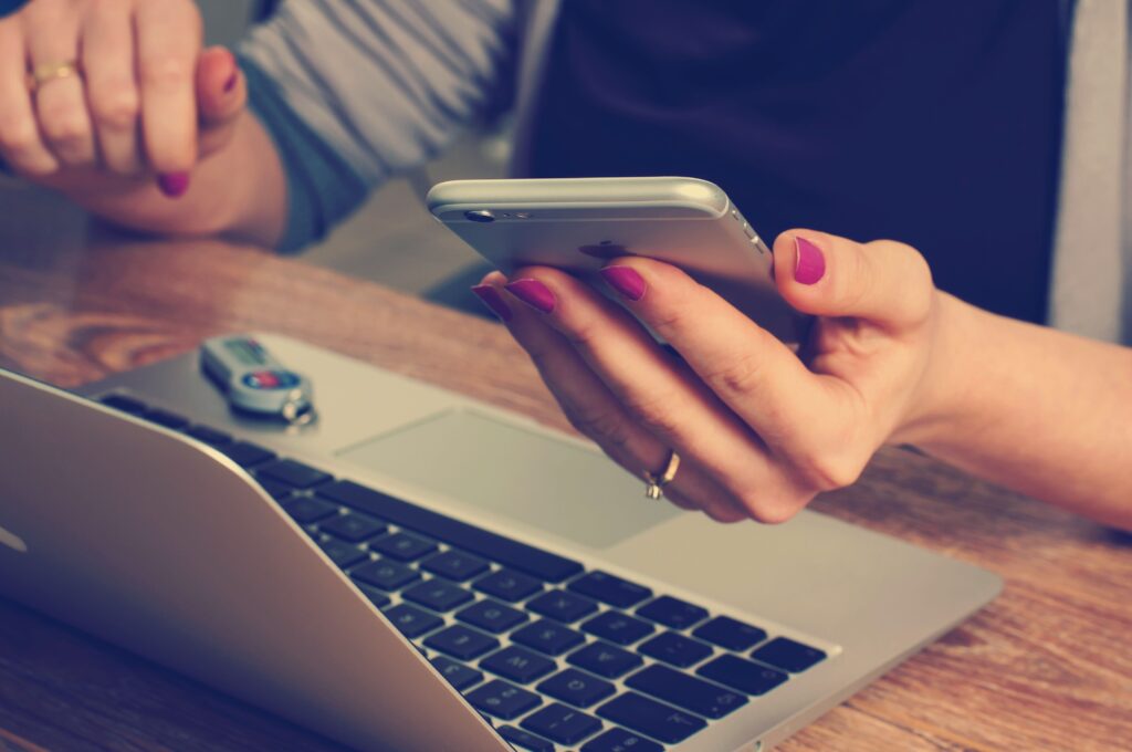 Close-up of a woman's hand holding a cellphone over a laptop computer.