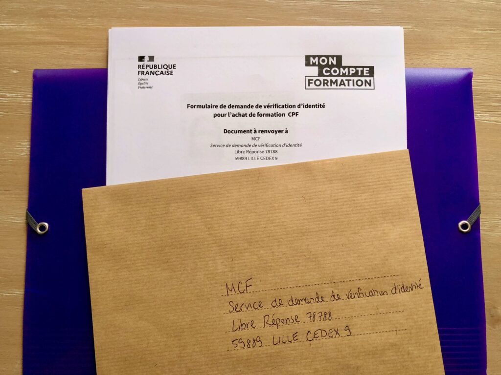 A stack of documents required to verify your identity in order to use your CPF (compte personnel de formation) account in France. Brown kraft envelope on top of the papers. Everything is resting on a purple folder.