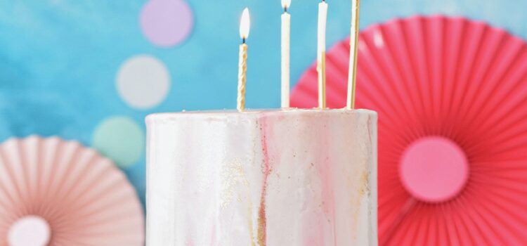 4 candles on a pink birthday cake with white and gold icing dripping down the sides