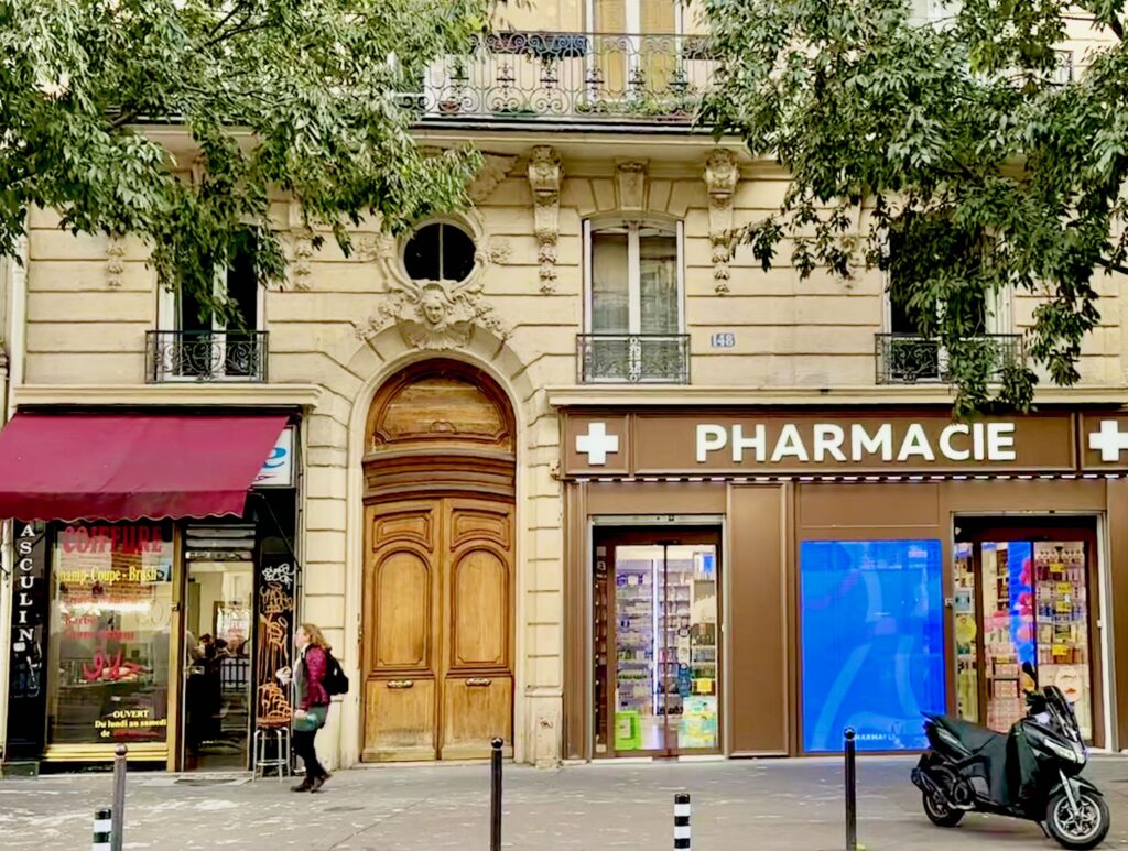 Paris façade showing a small hairdressing salon, a tall wooden door, and a pharmacy