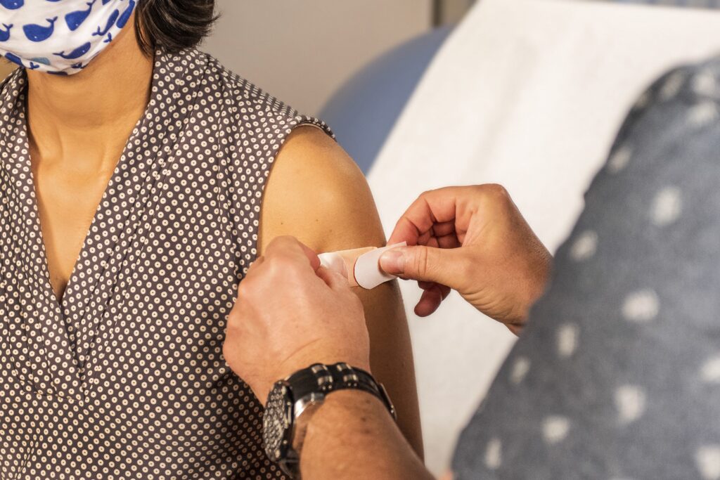 A health professional is applying a bandaid to a woman's upper arm following a vaccine injection