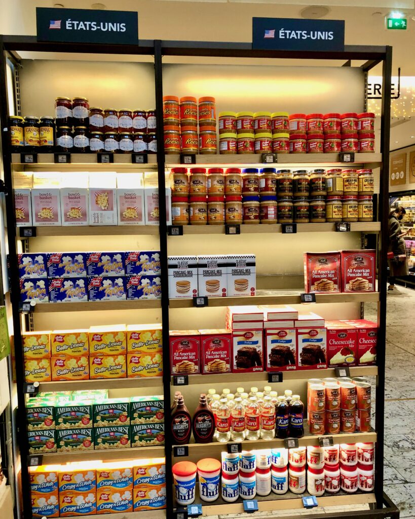Shelves full of U.S. American products in a Parisian grocery store (La Grande Épicerie de Paris) including peanut butter, microwave popcorn, brownie mix, corn syrup, canned pumpkin, and marshmallow fluff
