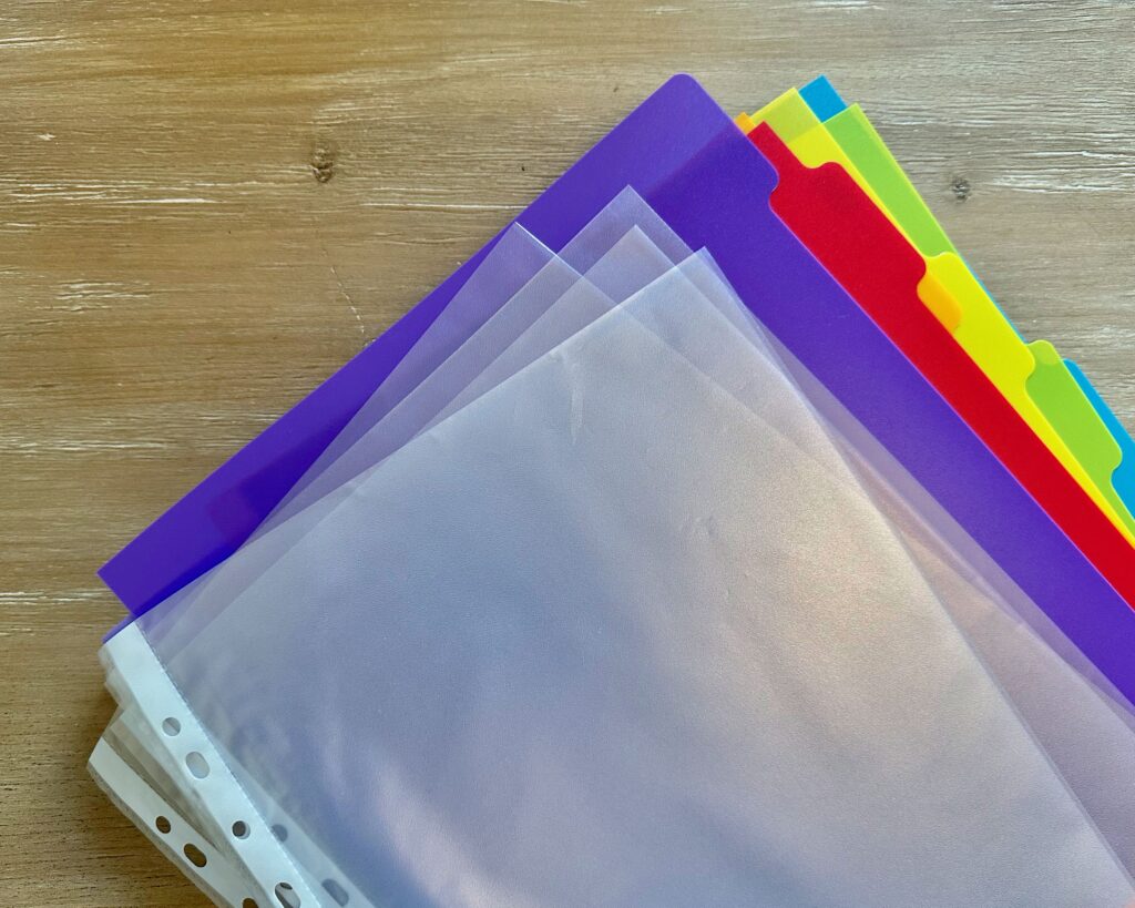 a stack of perforated sheet protectors on top of a stack colored divider tabs for organizing a binder