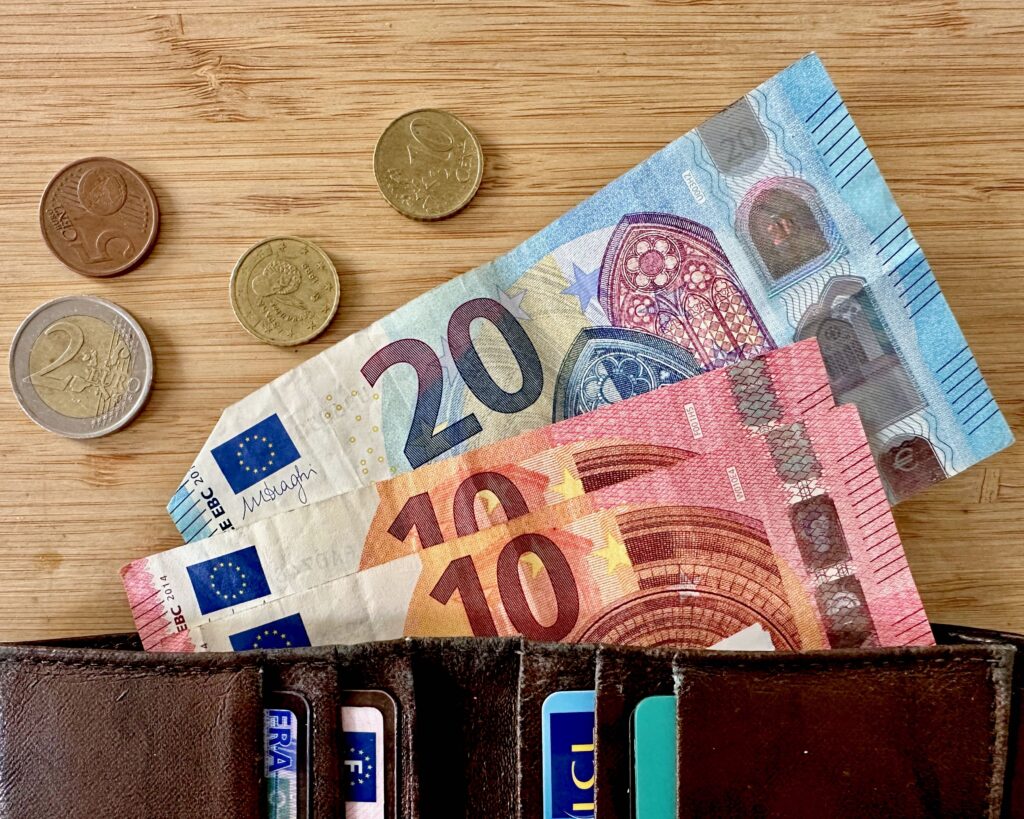 Euro coins and bills spilling out of a brown wallet