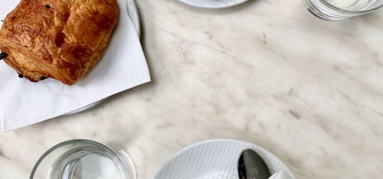 aerial view of two coffees, two glasses of water, and a pain au chocolat on a white marble table on a terrace in Paris