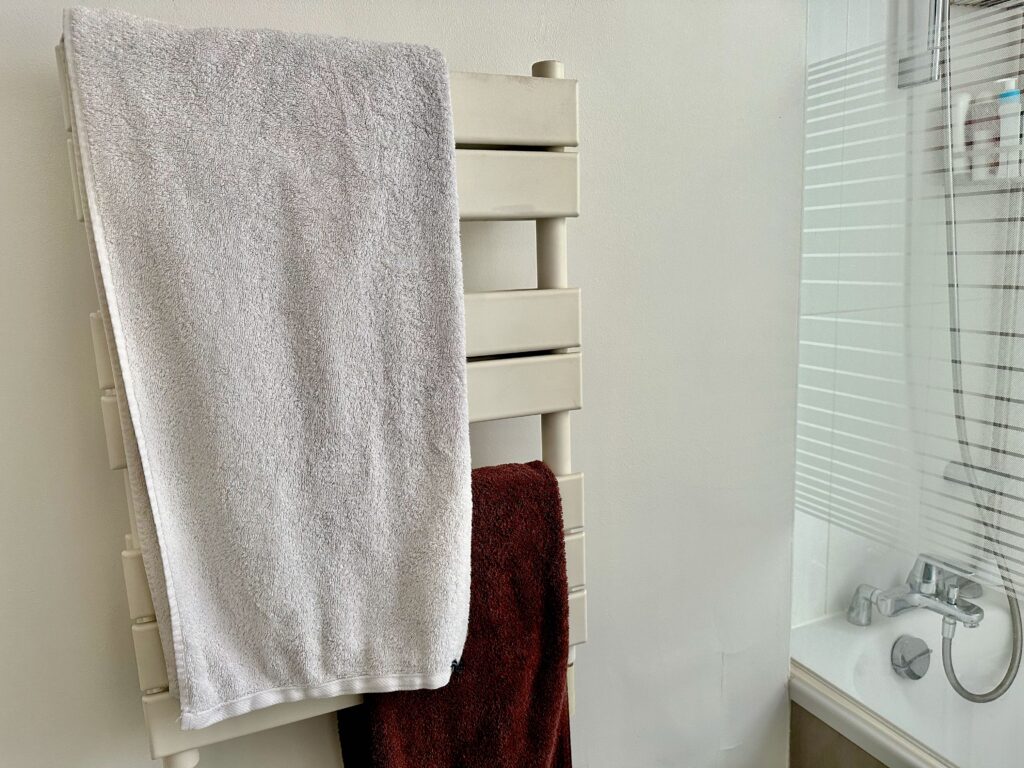 white towel warmer rack in a Parisian apartment bathroom with one folded white towel and one folded brown bath towel