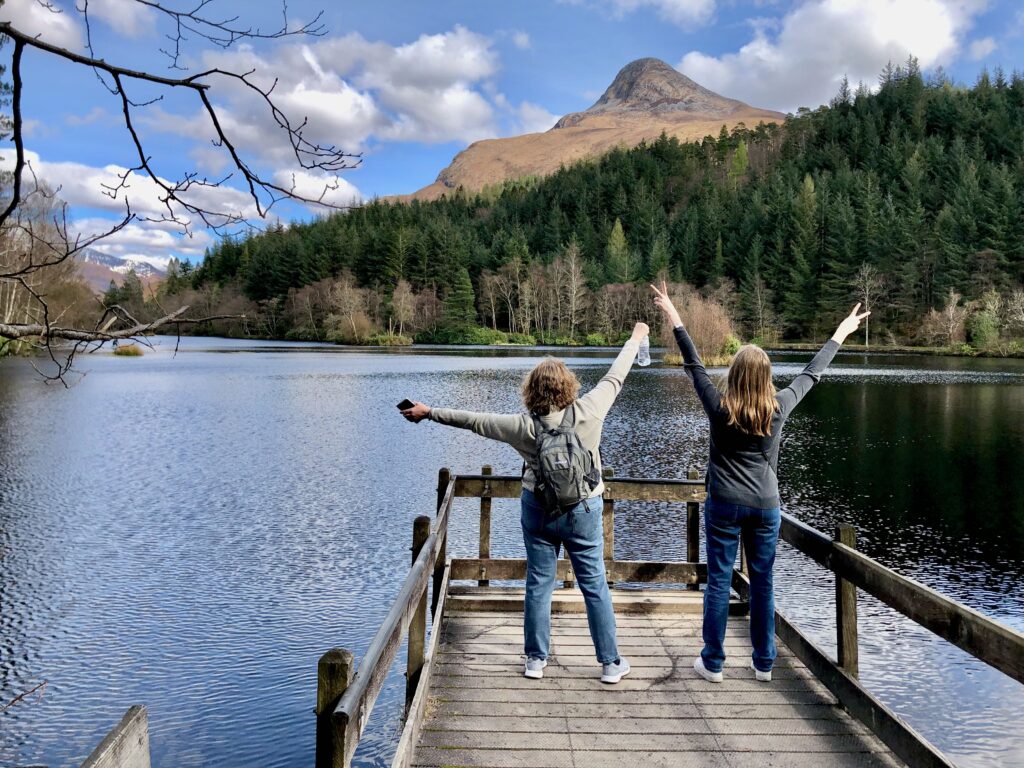 Two American women abroad in Scotland, visiting Glenco Lochan, facing the lake with backs to the camera