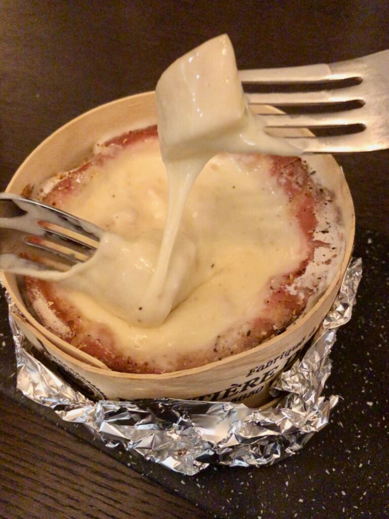 Two forks dipping potatoes into a melted Mont d'Or cheese