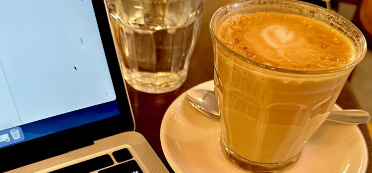 The Tough Realities of Being Self-Employed in France Latte next to an open laptop in a Paris coffee shop
