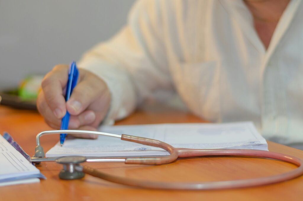 Medical professional filling out paperwork at a desk with a stethoscope next to the papers