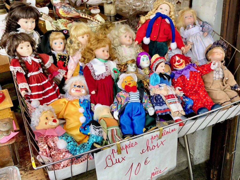 A selection of porcelain dolls and clowns in a basket at a Paris flea market