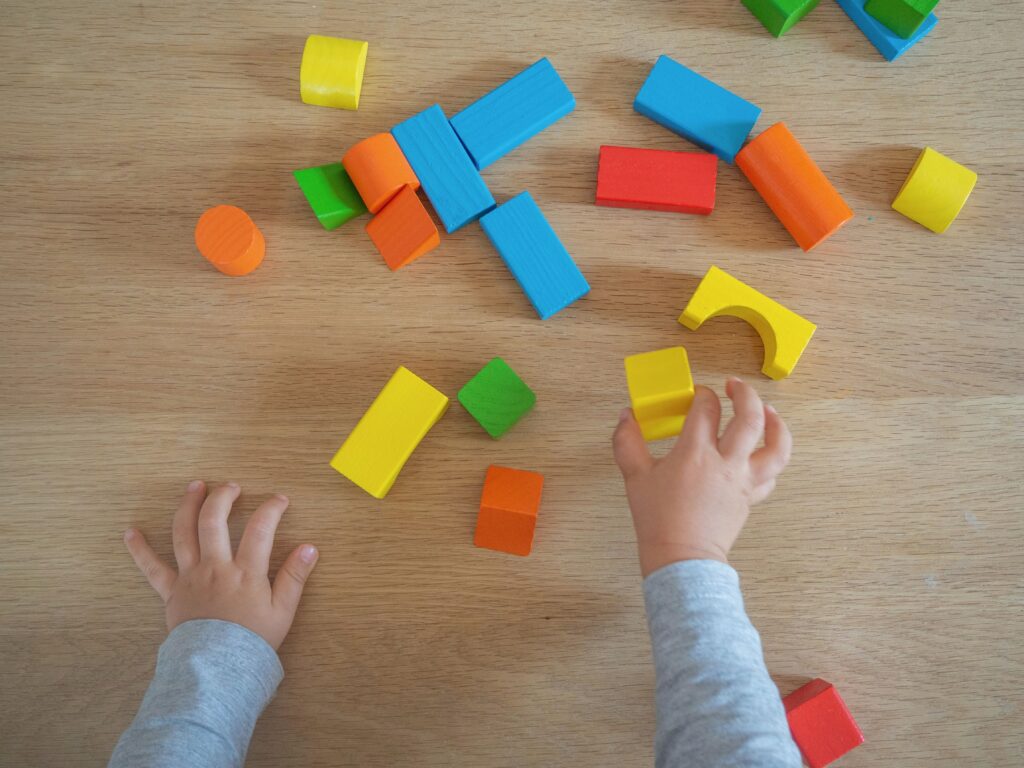 Two toddler hands reaching for colorful blocks sprawled out on the floor