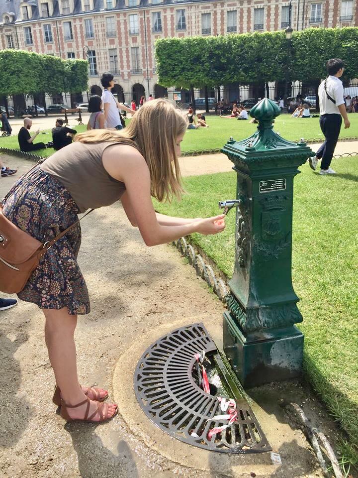Woman getting a drink of water from a green Wallace fountain in Place des Vosges on a hot day.