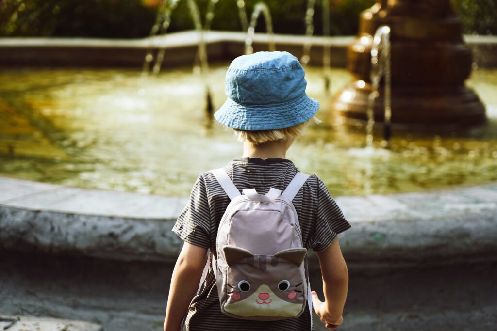 Toddler with backpack facing a fountain